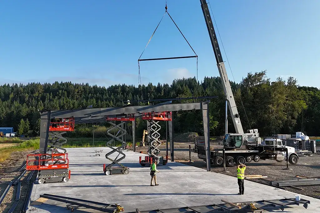 Westmore Construction team using a crane and scissor lifts to assemble a steel building frame at a job site.