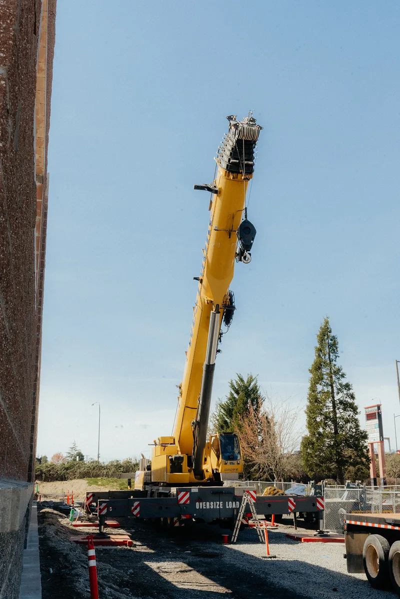 Westmore yellow Grove crane with an Oversize Load banner beside a brick building