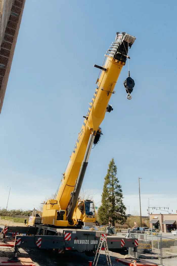 Westmore yellow Grove crane with the boom raised and the hook block beside a CMU wall