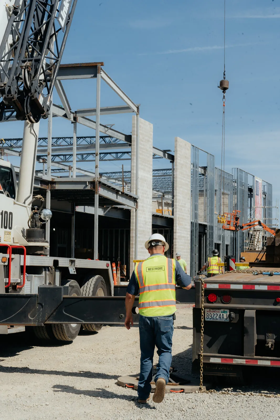 Westmore crew member walking past crane outriggers toward a steel building frame