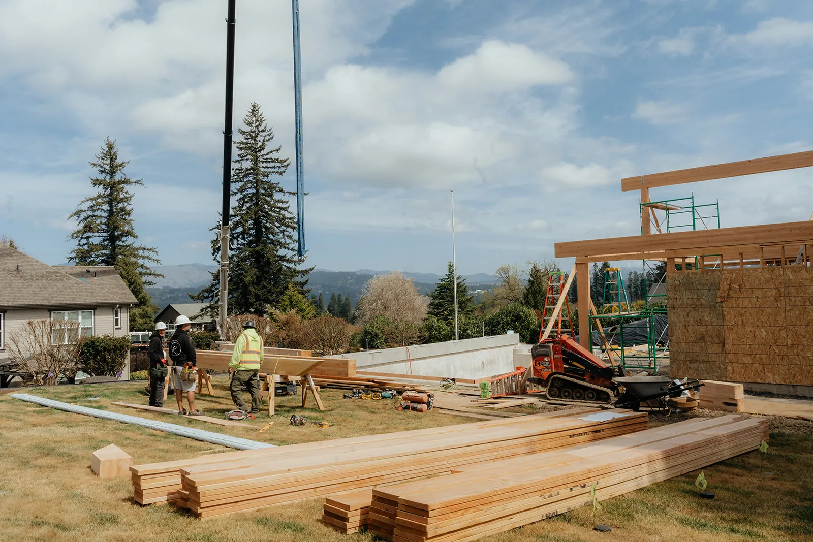 Crane cable lifting material at a timber-frame job site with lumber staged nearby