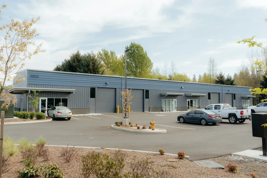 Completed gray metal commercial building with a parking lot in front, wide view