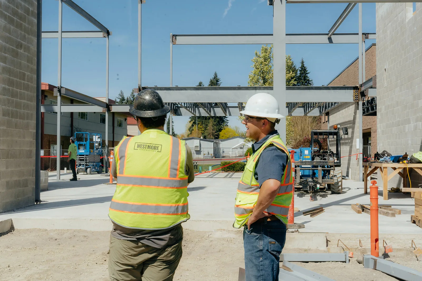Two Westmore crew members in hi-vis walking toward a steel frame at a commercial jobsite