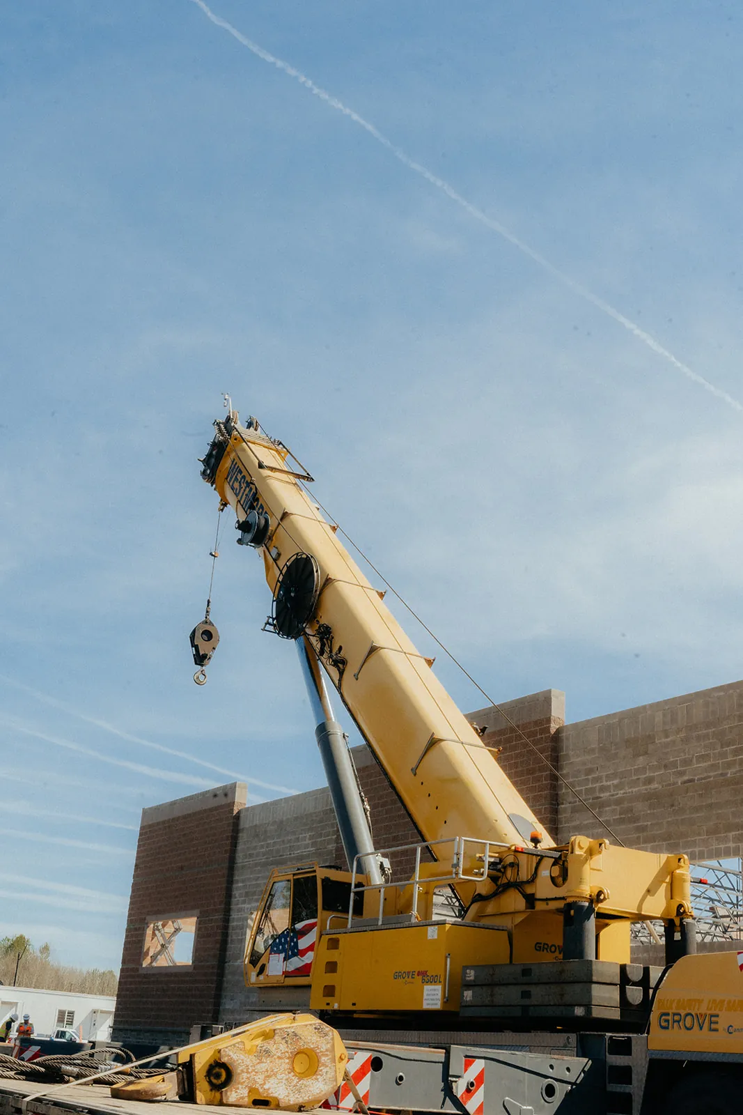 Yellow Grove crane hook block and boom over a CMU wall