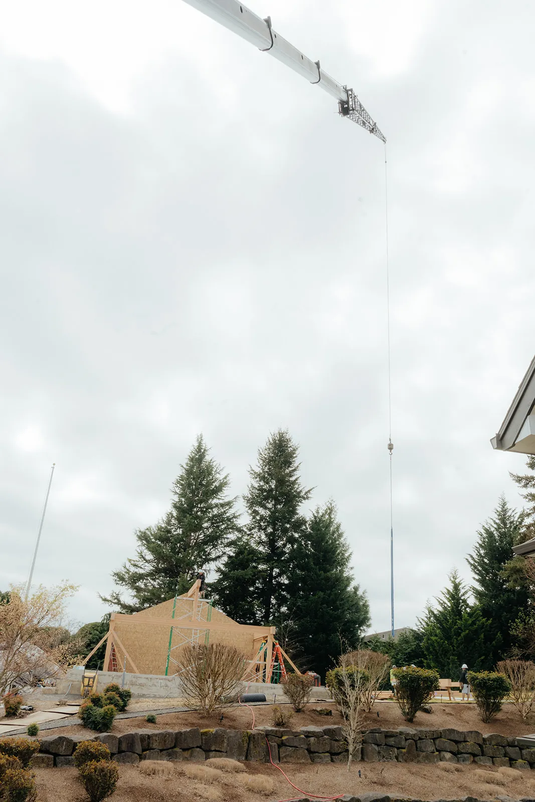Crane line lowering a timber pavilion frame into a residential backyard