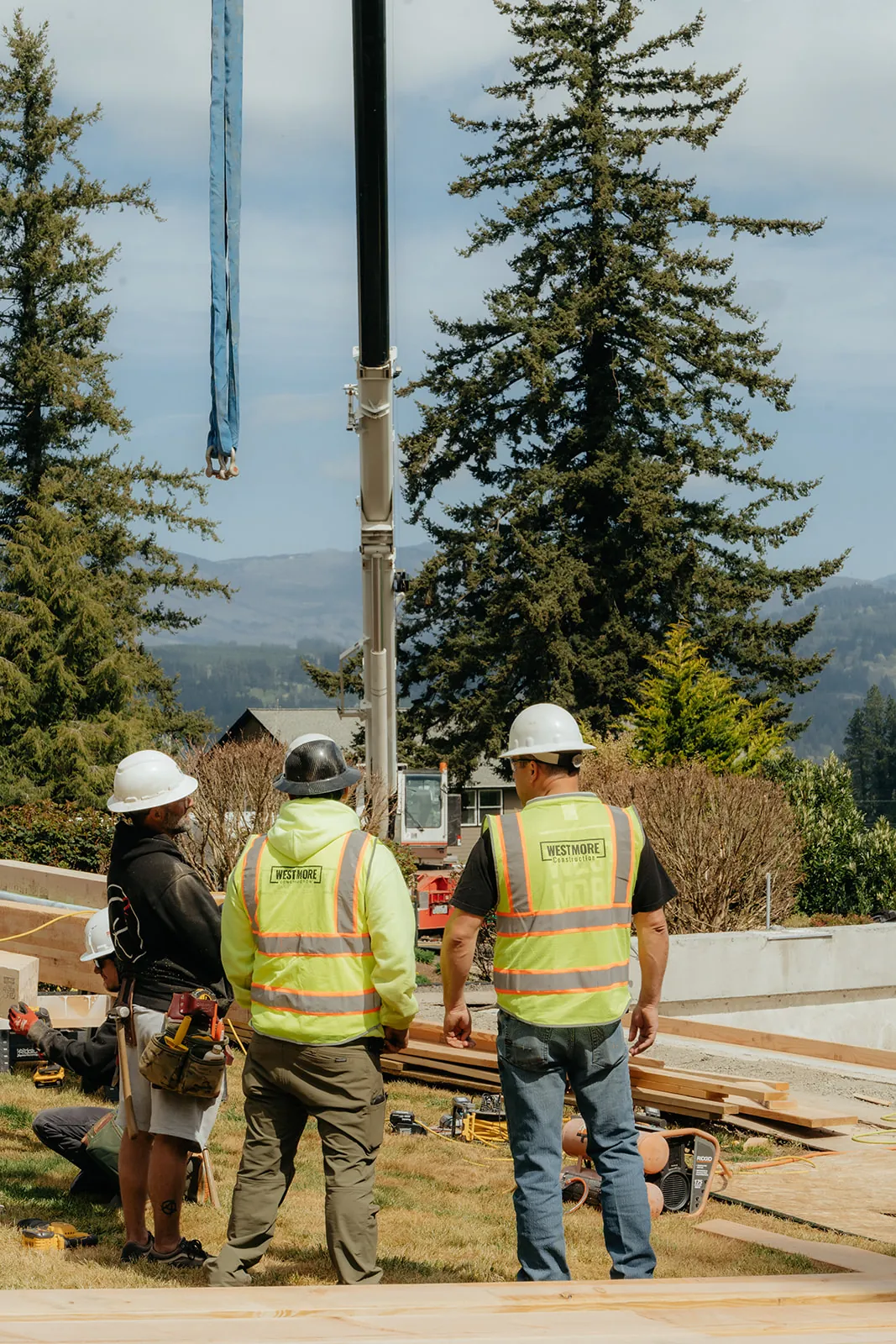 Three Westmore crew members guiding a crane line at a residential timber-frame job