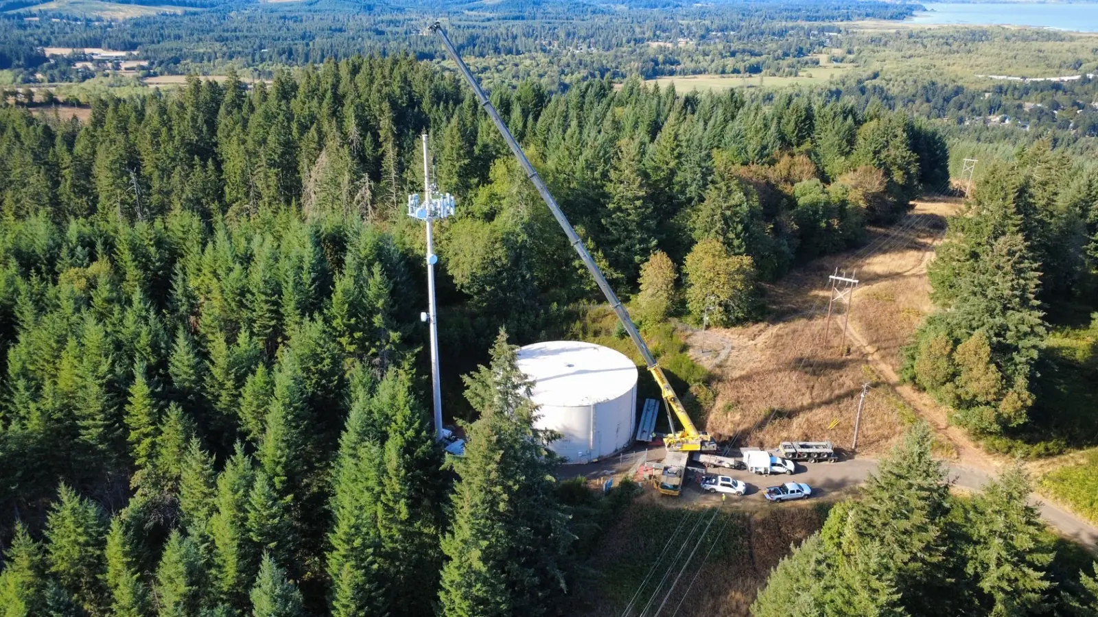 Aerial view of a Westmore crane set up beside a hilltop water tank and cell tower in the trees