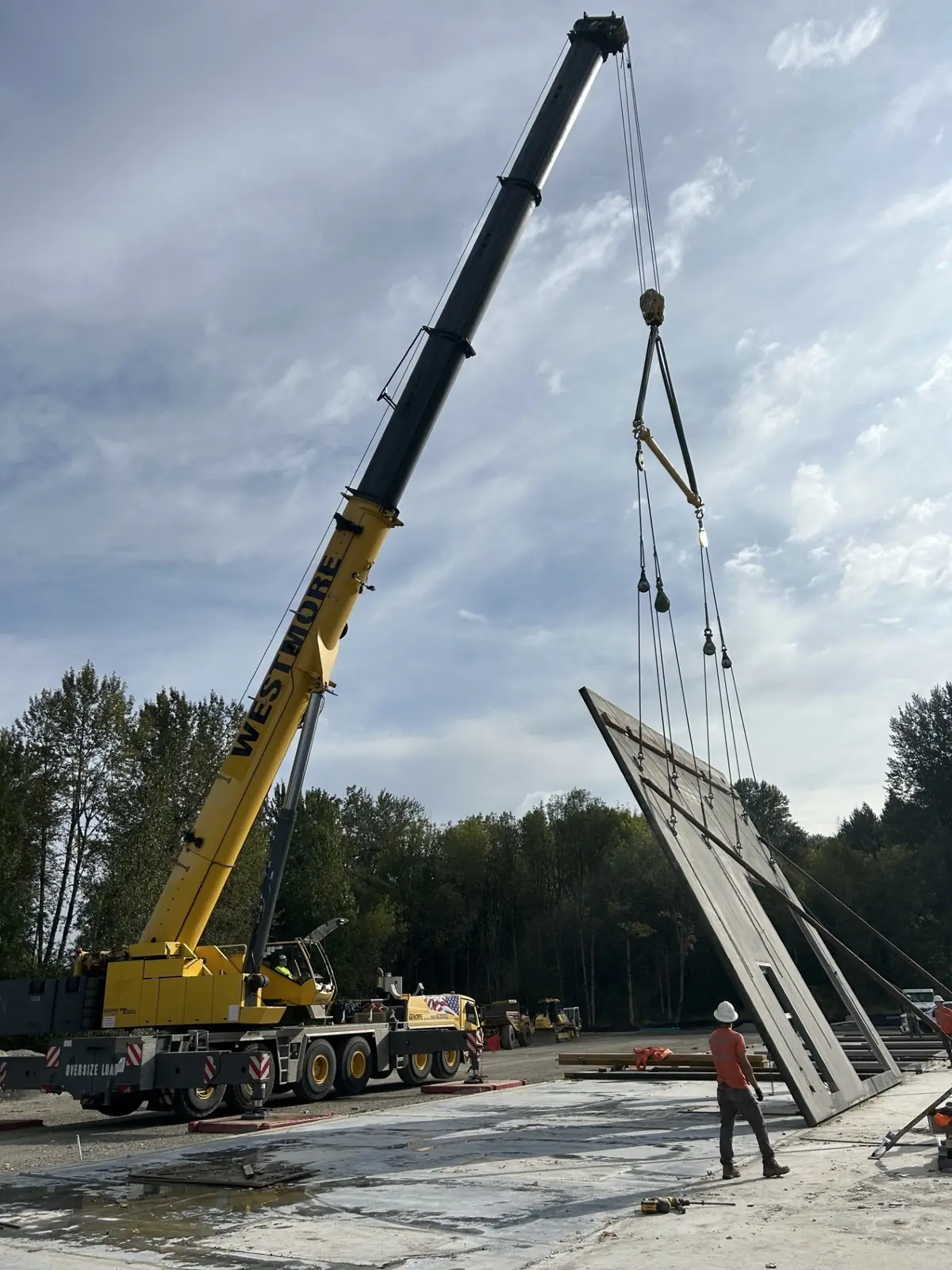 Westmore Grove crane tilting a concrete panel upright with a spreader bar as a crew member guides it