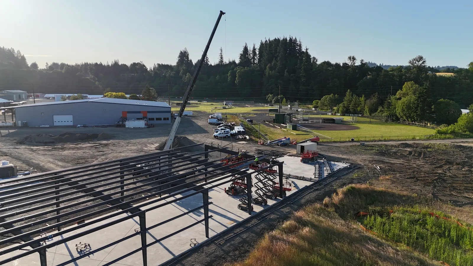 Aerial view of a pre-engineered steel building frame going up with the crane boom raised behind it